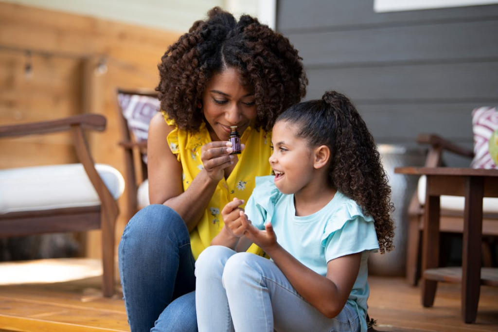 A mother with curly hair inhaling fragrance with her daughter sitting beside her 