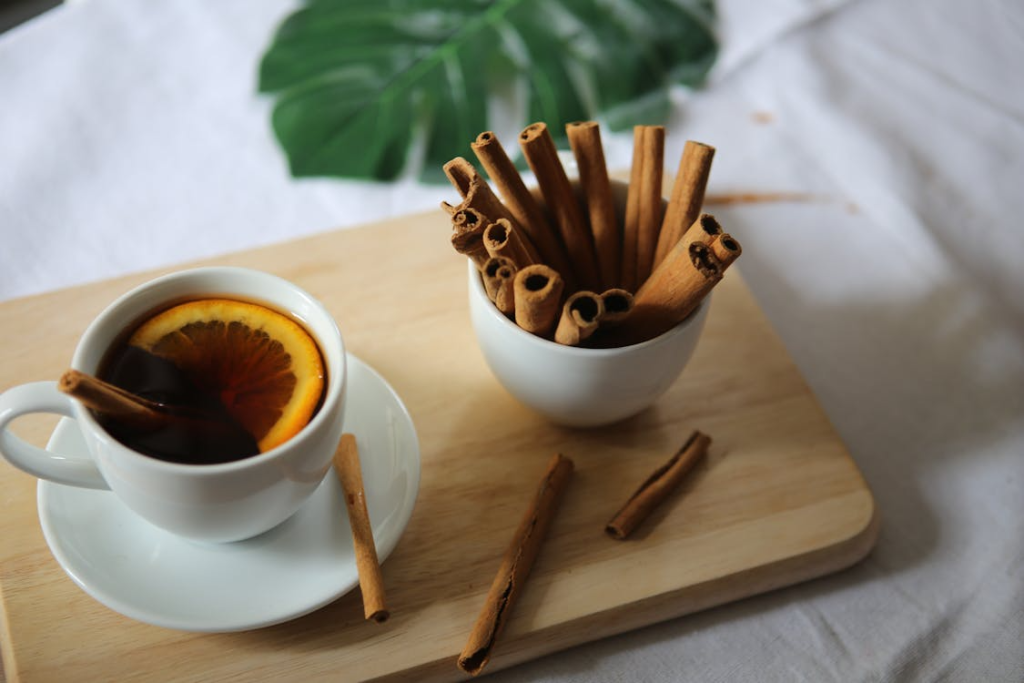 A cup of tea with infused lemon and whole cinnamon with a bowl of cinnamon sticks by the side