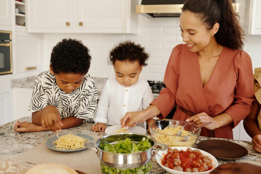 a mom serving food prepared using cold-pressed oils to her two boys sitting on the dining table in the kitchen